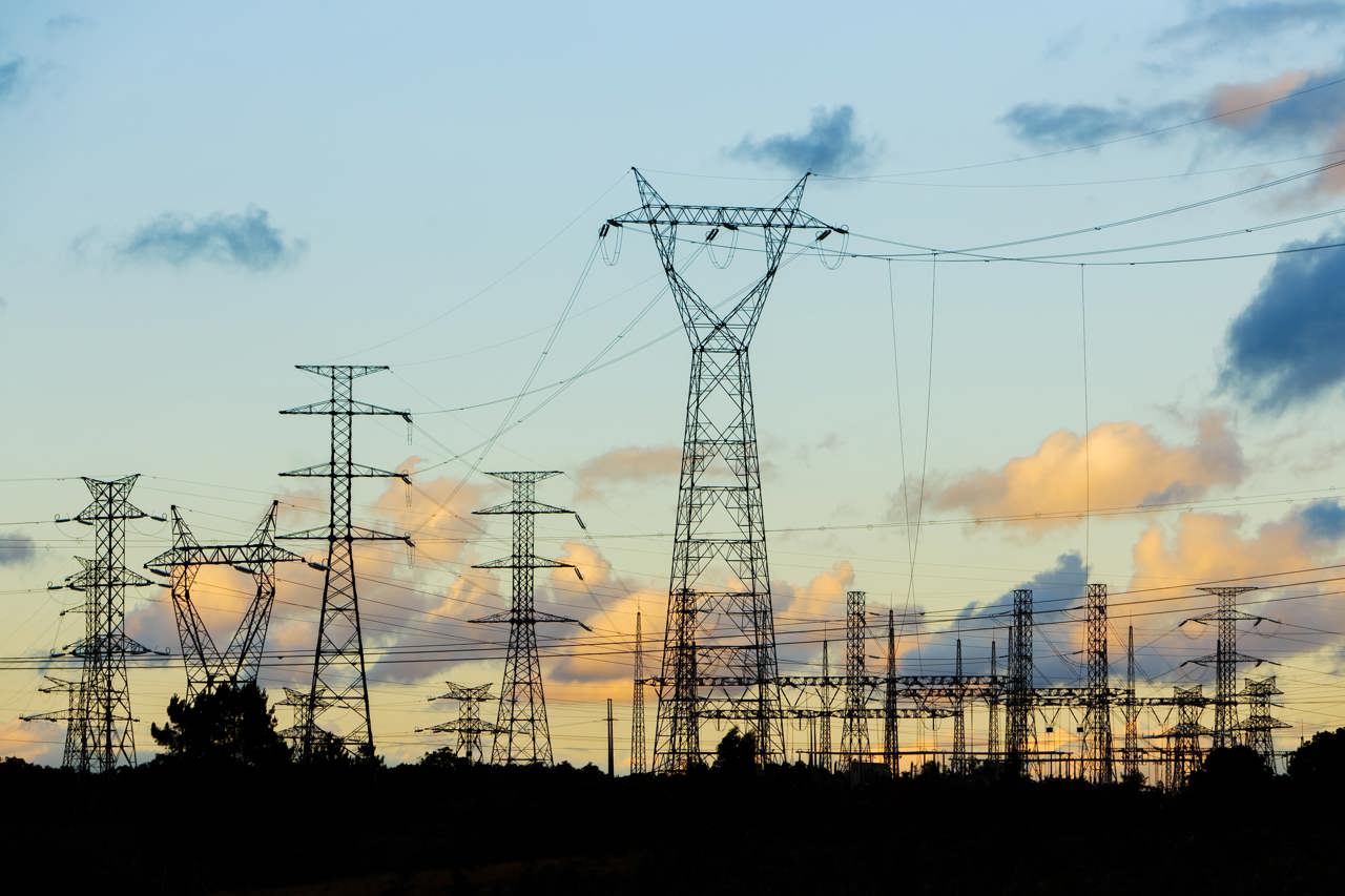 Very high voltage lines and pylons on REN's electricity transmission grid in the late afternoon, against an orange sky